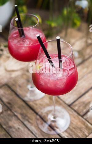 cocktail rosso con ghiaccio in vetro con gambo su superficie di legno Foto Stock