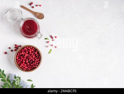 Concetto piatto con marmellata di mirtilli fatti in casa e cowberry foresta in ciotola su tavolo bianco con tovagliolo blu. Foto Stock