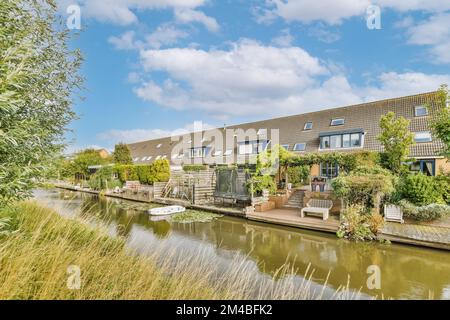 alcune case sul lato di un corpo d'acqua con alberi e cespugli in fronte - area crescente accanto ad esso Foto Stock
