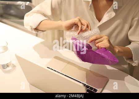 La donna sta aprendo pacchetti che sono avvolti in bolle d'aria mentre si siede di fronte al notebook Foto Stock