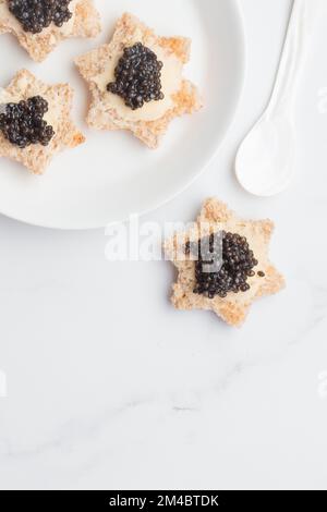 Antipasti neri al caviale stelle del pane con burro su sfondo bianco vista dall'alto verticale Foto Stock