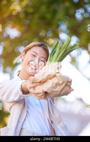 Alimentari, shopping bag e donna asiatica con verdure in città dopo l'acquisto di piante sane o nutrienti sul mercato. Benessere, offerte di vendita e femminile Foto Stock