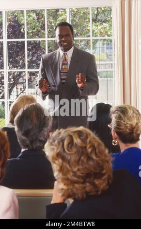 Uomo d'affari afro-americano di fronte a parlare con una stanza piena di persone Foto Stock
