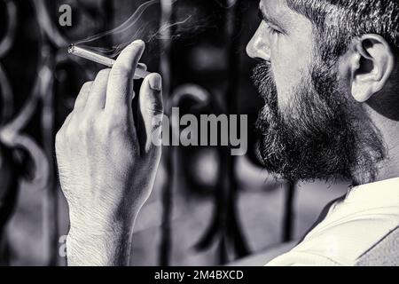 Uomo che fuma con barba. Il giovane uomo di hippster fuma. Bianco e nero Foto Stock