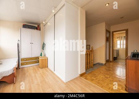 Uno spazio aperto con armadi a muro, un piccolo letto e accesso alle scale in una casa indipendente a più piani Foto Stock