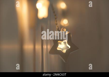 Luci di Natale a forma di stella Garland appeso su una parete di legno. Primo piano, messa a fuoco selettiva. Interno della camera da letto. Accogliente momento di casa. Capodanno, umore di Natale Foto Stock