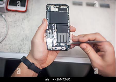 Riparazione del telefono cellulare presso il centro di assistenza, smontaggio e diagnostica dello smartphone, vista dall'alto del luogo di lavoro del riparatore Foto Stock