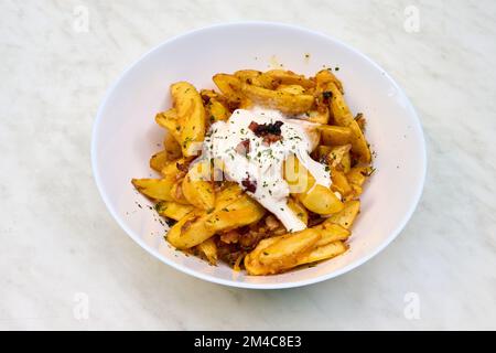 Un primo piano di spicchi di patate in un piatto bianco con salsa cremosa Foto Stock
