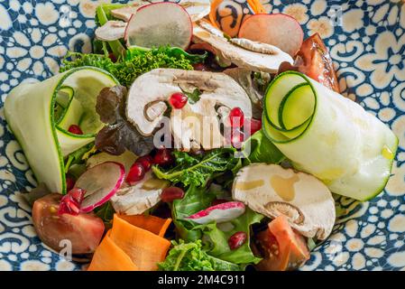 Una deliziosa insalata di verdure con fettine di zucchine e carote, foglie di kale, fettine di funghi, semi di melograno, pomodoro e ravanello Foto Stock