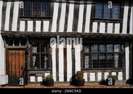 Appoggiandosi a destra: Piano superiore a graticcio di Box Cottage in Prentice Street, Lavenham, Suffolk, Inghilterra, Regno Unito. La casa, costruita negli anni '1400s o '1500s, sorge su un alto zoccolo di mattoni e presenta bifore in rovere, luci a piombo, travi a vista e travetti e una finestra a tre luci sullo specchio di poppa sopra la sua porta anteriore. Foto Stock