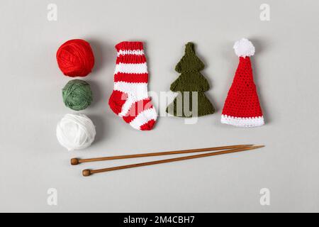 Calzini di Natale rossi e bianchi lavorati a maglia, cappello di Babbo Natale e albero verde con una palla bianca e rossa di fili e aghi da maglieria. Decorazione di Natale Foto Stock