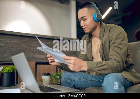 Dipendente asiatico concentrato che legge i documenti nelle sue mani Foto Stock