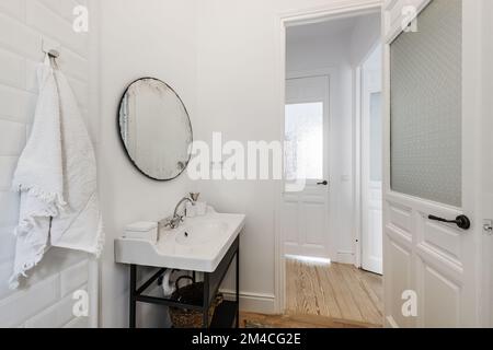 Bagno in stile vintage con lavello in porcellana su armadio in metallo, specchio circolare e porta in legno massiccio con vetro traslucido Foto Stock