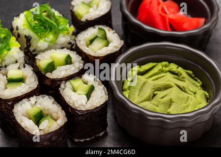 Sushi con cetriolo e alghe. Wasabi in una ciotola nera. Primo piano. Sfondo nero. Foto Stock