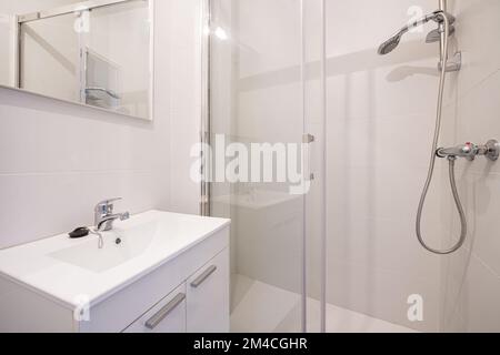 Piccolo bagno con armadi in legno laccato bianco con porte, specchio senza cornice a parete, infissi in acciaio inossidabile, lavello in porcellana e cabina-in spettacolo Foto Stock