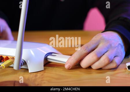 inserimento di un modem gsm in un router bianco con due antenne su un tavolo di legno da parte di una persona in un felpa nera Foto Stock