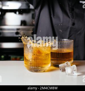 i cubetti di ghiaccio cadono in un bicchiere di whisky Foto Stock