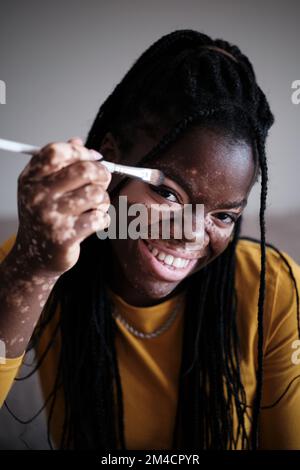 Donna nera allegra con la pelle di vitiligo che fa il trucco Foto Stock