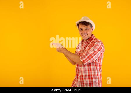 Uomo in cappello e camicia colorata a scacchi che indica il lato con le mani su uno sfondo arancione Foto Stock