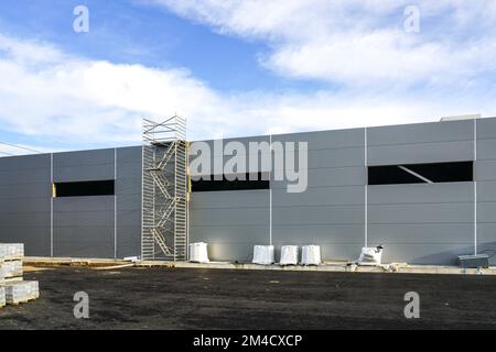 Facciata grigia a pannelli sandwich di un magazzino non finito, impalcatura tubolare multilivello, sfondo blu cielo Foto Stock