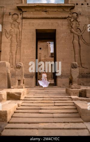 Una foto verticale di una donna in un abito bianco che si erge all'ingresso del complesso del tempio di Philae. Foto Stock