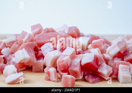 primo piano di pancetta affumicata salata a dadini pancetta di maiale lardons su un tavolo da taglio di bambù sfondo bianco Foto Stock