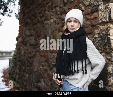 Ritratto medio di una ragazza in abiti caldi e morbidi sullo sfondo di un vecchio muro di mattoni Foto Stock