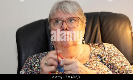 Donna anziana che si inginocchiava e guardava la TV allo stesso tempo Foto Stock