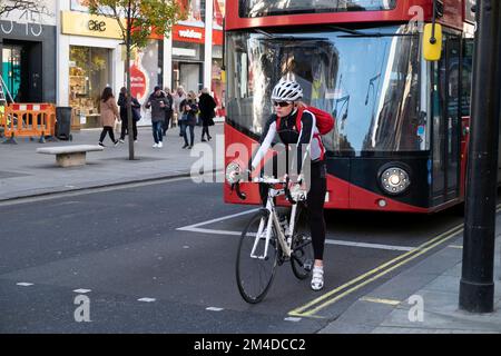 Giovane donna ciclista donna in attesa al segnale del traffico davanti a un autobus a due piani rosso su Oxford Street West End Londra UK Inghilterra KATHY DEWITT Foto Stock