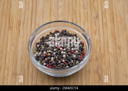 Una miscela di peperoni in una ciotola di vetro closeup su sfondo di legno Foto Stock