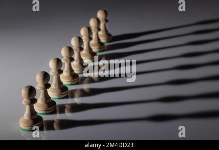 Linea diagonale di pedine di scacchi in legno bianco con messa a fuoco selettiva e gioco d'ombra sul pavimento Foto Stock