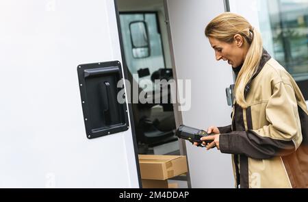 l'agente di consegna tiene il lettore di codici a barre fuori dal furgone per controllare i pacchi Foto Stock