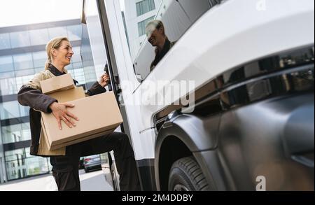 agente di consegna che tiene pacchi da un furgone per consegnarli a un cliente Foto Stock