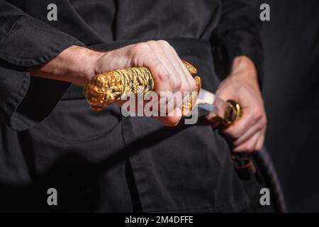 Il samurai che tiene una spada katana giapponese. Foto di un guerriero vestito con abiti neri in basso con messa a fuoco selettiva Foto Stock