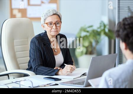 Ritratto di donna d'affari matura indossando occhiali che parlano con il dipendente in riunione, copia spazio Foto Stock