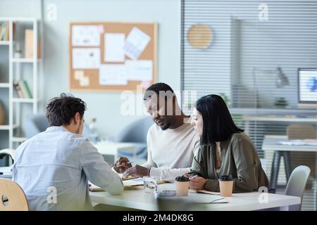 Team aziendale multietnico di tre persone che discutono il progetto durante la riunione in carica Foto Stock