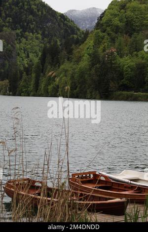 Ormeggiata barca di legno su un lago con la foresta innevata e verde sullo sfondo in una giornata di pioggia. Foto Stock