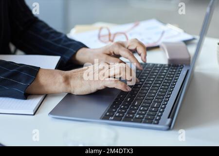 Primo piano delle mani femminili senior che scrivono sulla tastiera del computer portatile mentre lavorano in ufficio, in ufficio, in ufficio Foto Stock