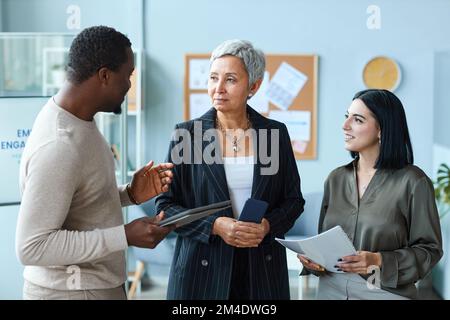 Vita in su ritratto di donna d'affari anziana che parla con i dipendenti mentre in piedi in ufficio Foto Stock