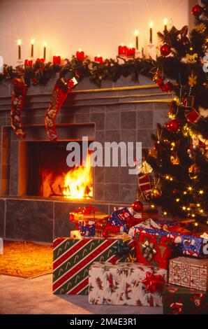 Fotografia di natura morta di stanza decorata con albero di Natale, camino, regali e calze appese al mantello e candele Foto Stock