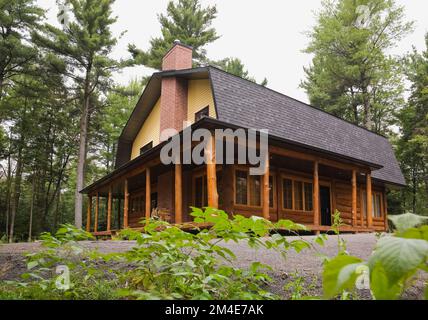 Casa in legno in stile cottage ibrido con clapboard giallo e tetto mansardato in asfalto sfumato grigio. Foto Stock