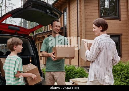 Ritratto di famiglia felice che scarica le scatole dal tronco dell'automobile mentre si sposta in nuova casa in natura Foto Stock