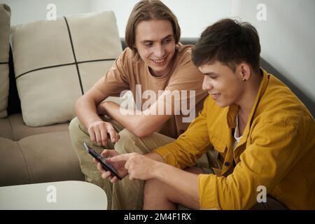 Giovane uomo allegro che mostra la foto della sua ragazza su smartphone ad un amico Foto Stock