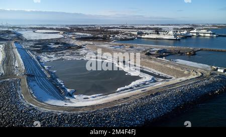 Fehmarn, Germania. 16th Dec, 2022. La fossa di scavo per il portale del tunnel al tunnel di Fehmarnbelt è visibile accanto al porto di lavoro e al porto dei traghetti di Puttgarden (fotografia aerea scattata con un drone). Il tunnel ferroviario e stradale di 18 km collegherà l'isola di Fehmarn e l'isola danese di Lolland dal 2029. Secondo Femern A/S, il costo è di 7,1 miliardi di euro. Credit: Christian Charisius/dpa/Alamy Live News Foto Stock