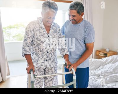 Piccoli passi mio caro. una donna matura determinata che usa una struttura ambulante per camminare con mentre è sostenuta da suo marito nel paese durante il giorno. Foto Stock