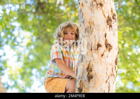 ragazzo di 8 anni che si arrampica su un albero alto nel parco. Superare la paura delle altezze. Buona infanzia. Capretto che cerca di arrampicarsi sull'albero. Foto Stock