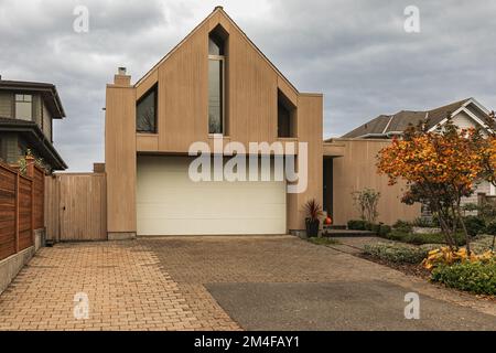 Vista esterna della casa moderna con garage decorato con legno. Immobiliare di lusso casa singola familiare con facciata in legno. Casa residenziale con moder Foto Stock