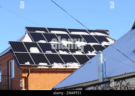Pannelli solari innevati sono montati sul tetto di una casa privata. Energia alternativa in inverno Foto Stock