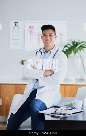 Entra nel mio ufficio. Ritratto corto di un giovane medico maschio seduto con le braccia ripiegate in un ospedale. Foto Stock