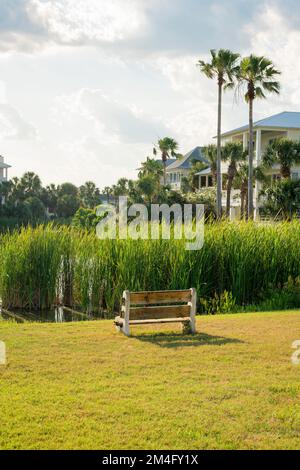 Piccola panca di fronte alle alte erbe del lago, davanti alle case di Destin, Florida. Panchina su un campo in riva al lago e vista di tre Foto Stock